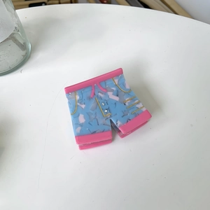 Détail de la pince à cheveux en acétate en forme de short bleu et rose avec des strass fins