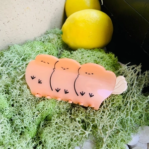 Close-up of peach acetate hair claw clip with cartoon chick patterns on green moss
