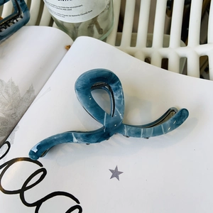 Dettaglio molletta per capelli blu marmorizzato con design a onda su un libro bianco