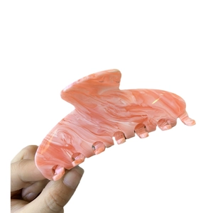 Grande pince à cheveux en acétate motif marbre rose et blanc tenue à la main sur fond blanc