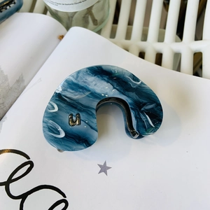 Dettaglio della molletta per capelli in acetato con trama marmo blu e accento dorato in U