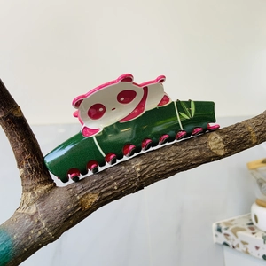 Detalle de pinza de pelo panda de acetato en una rama con dientes rosa brillantes