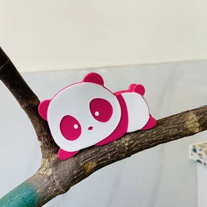 Detalle de pinza para el pelo de panda en acetato rosa y blanco sobre una rama de madera