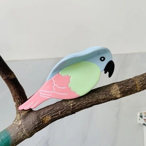 Chic parrot-shaped acetate hair claw in blue, green, and pink on a tree branch