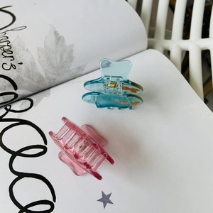Détail de pinces à cheveux bocal en acétate bleu et rose posées sur un magazine chic