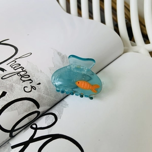 Pince à cheveux en acétate bleu design aquarium avec poisson sur un magazine