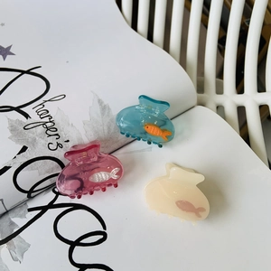 Trois pinces à cheveux bocal à poisson en acétate bleues, roses et blanches sur revue