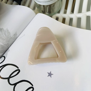 Close-up of matte beige triangular hollow hair claw clip on white magazine background