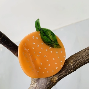Acetate orange fruit hair claw clip with green leaves on a natural wood branch