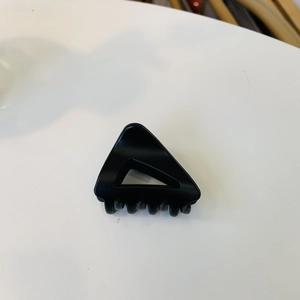Détail d'une pince à cheveux triangulaire noire évidée sur une surface blanche unie
