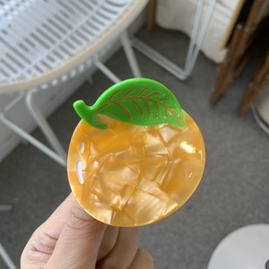 Vibrant orange acetate hair claw clip in fruit shape with green leaf detailing