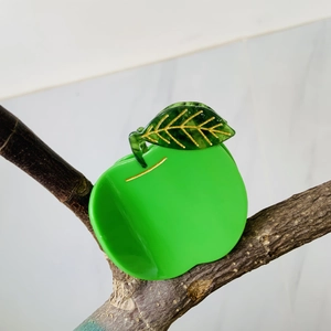 Detailed close-up of a green apple hair claw clip featuring golden leaf veins on white marble