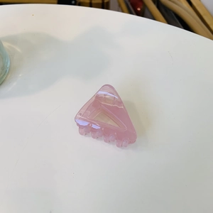 Détail d'une pince à cheveux triangulaire en acrylique rose avec finition brillante et ressort