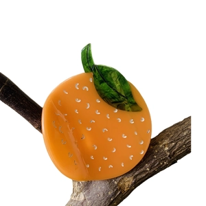 Vibrant orange-shaped acetate hair claw clip with green leaf on a wooden branch