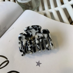 Detailed macro view of black and white marble acetate hair claw clip with golden lettering