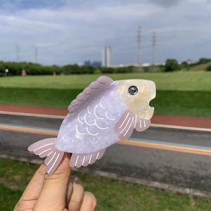 Vue détaillée d'une grande pince à cheveux poisson en acétate marbré rose tenue à la main