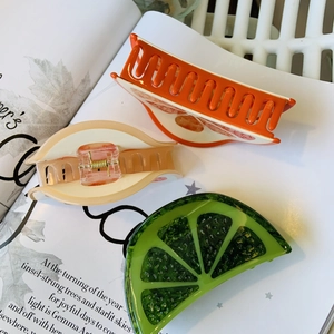 Detail view of acetate fruit hair claws featuring orange and lime patterns on a magazine