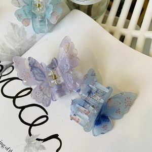 Détail des pinces à cheveux papillon en acrylique avec motifs floraux pailletés et ressort doré