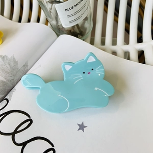 Gros plan d'une pince à cheveux chat en acétate bleu clair posée sur un livre ouvert