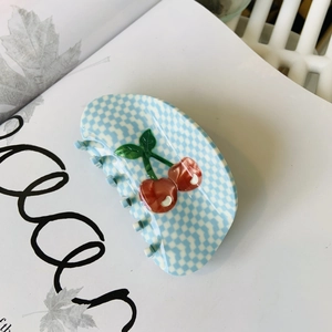 Gros plan d'une pince à cheveux à carreaux bleus ornée de cerises 3D sur un livre blanc