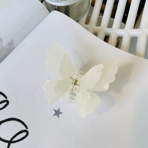 Detail shot of a white pearlescent butterfly hair claw clip with golden metal spring