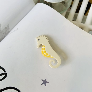 Macro detail of a beige acetate seahorse hair claw clip with yellow plaid patterns