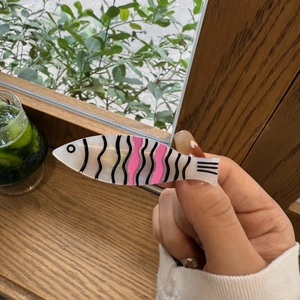 Gros plan d'une pince à cheveux en acétate en forme de poisson avec motifs ondulés roses