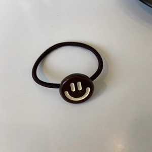 Elastico per capelli marrone Y2K con ciondolo a faccina gialla su una superficie bianca