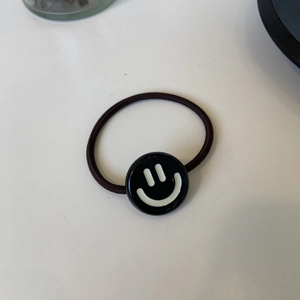 Dettaglio dell'elastico per capelli con ciondolo nero a forma di faccina sorridente