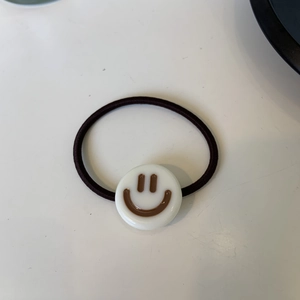 Dettaglio dello charm in acetato bianco con faccina sorridente marrone su elastico nero