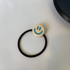Dettaglio dell'elastico per capelli nero con ciondolo a faccina in acetato giallo