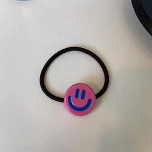 Dettaglio dell'elastico per capelli in acetato rosa con ciondolo a faccina blu e cordino nero