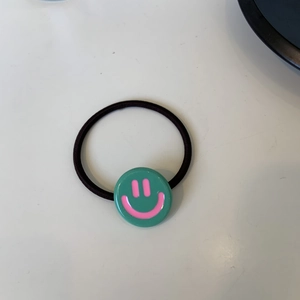 Dettaglio di un elastico per capelli verde con ciondolo a faccina rosa in stile Y2K