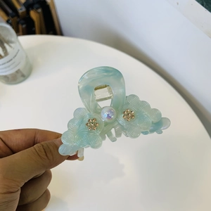 Detail of light blue cloud-shaped hair claw with iridescent finish and gold floral accents
