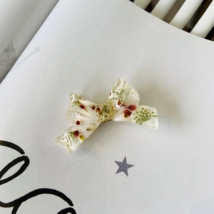 Floral resin bow hair clip with embedded dried flowers on white background