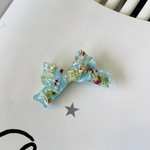 Detail shot of light blue resin bow hair clip with embedded colorful dried flowers