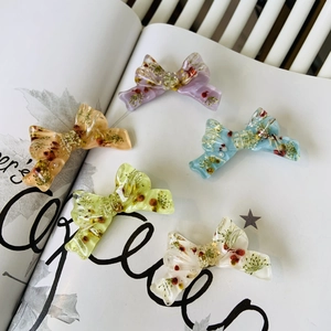 Detail view of five resin bow hair clips with real dried flowers and golden beads