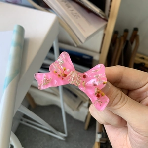 Detailed macro view of a pink resin bow hair clip with embedded dried flowers inside