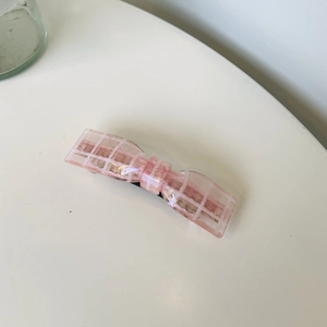 Détail d'une barrette à cheveux nœud rose à carreaux en acétate sur fond blanc