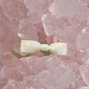 Barrette à cheveux nœud blanc avec texture nacrée et finition acétate sur fond de glace rose
