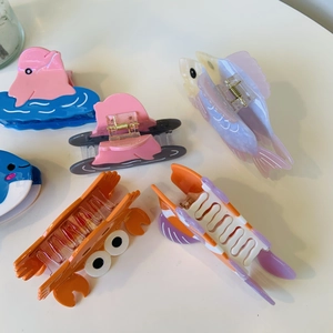 Dettaglio di mollette per capelli serie oceano in acetato con forme di granchio e delfino