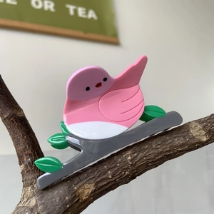 Detail of bird-shaped acetate hair claw clip with pink leaf accents on a natural branch