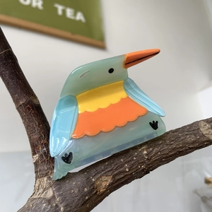 Detail view of bird-shaped acetate hair claw clip on a natural wooden branch