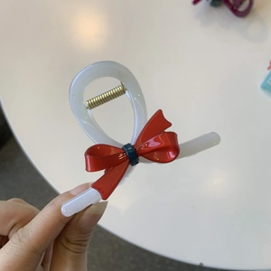 Detail of a white acetate hair claw clip featuring a bright red bow and golden spring