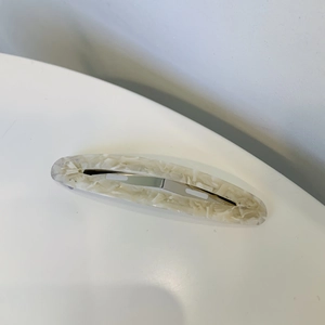 Détail de la texture marbrée d'une pince à cheveux ovale en acétate crème et fermoir argent
