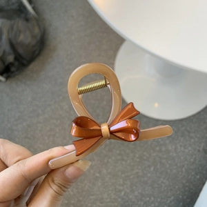 Detail of a beige hair claw clip with an orange bow and gold spring mechanism