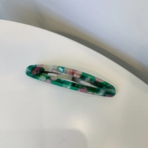 Détail de la texture marbrée verte et rose de la barrette ovale évidée en acétate