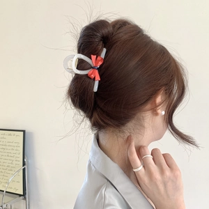 Elegant cream acetate hair claw clip with a red bow detail on a ponytail hairstyle