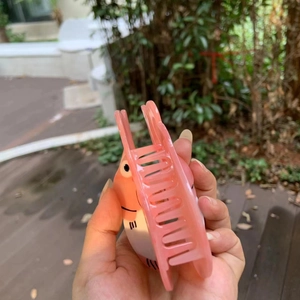 Detail of light pink Ponyo character claw clip held in hand with outdoor background