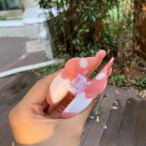 Pink and white marble acetate hair claw clip with metal spring held in a hand
